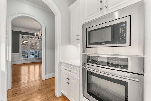 kitchen with an inviting chandelier, crown molding, light wood-type flooring, appliances with stainless steel finishes, and white cabinetry