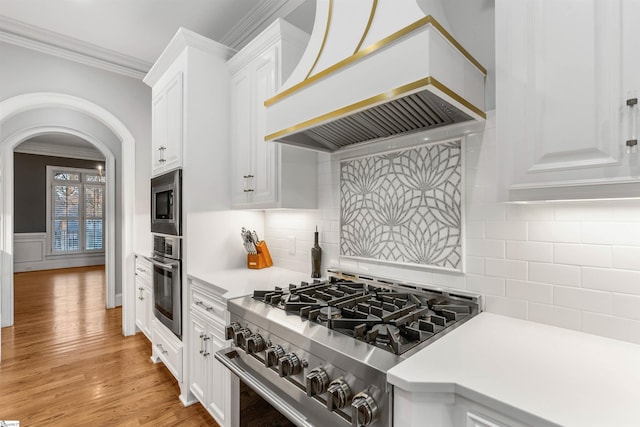 kitchen featuring light wood-type flooring, tasteful backsplash, custom exhaust hood, stainless steel appliances, and white cabinetry