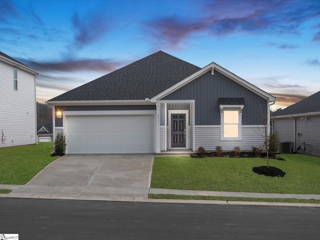 view of front of house with cooling unit, a garage, and a lawn