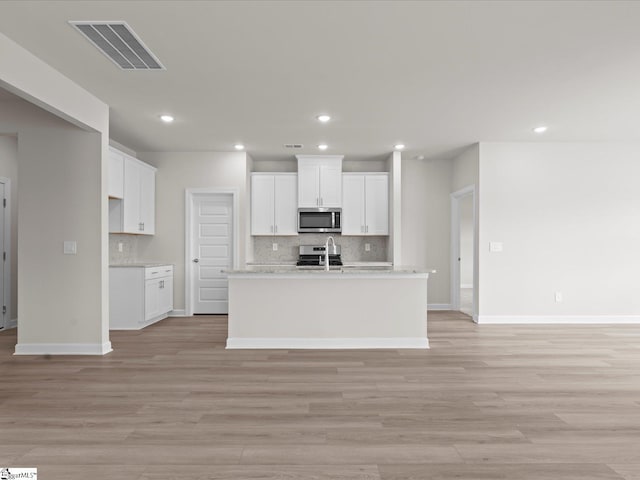 kitchen with white cabinetry, a kitchen island with sink, and light wood-type flooring