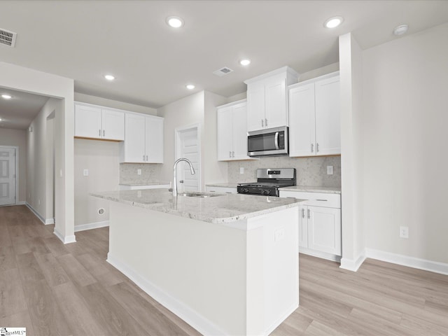 kitchen with stainless steel appliances, sink, an island with sink, and white cabinets