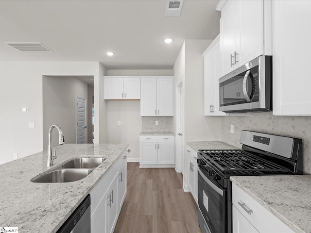 kitchen with light stone counters, appliances with stainless steel finishes, sink, and white cabinets