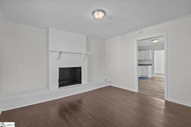 unfurnished living room with a textured ceiling, ornamental molding, dark hardwood / wood-style floors, and a brick fireplace