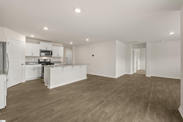 kitchen featuring dark hardwood / wood-style flooring, light stone counters, stainless steel appliances, white cabinets, and an island with sink