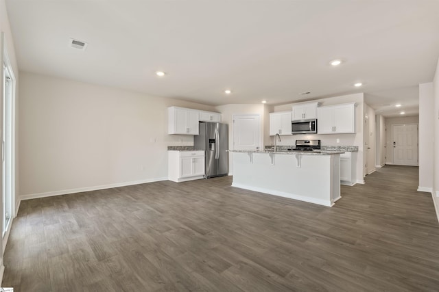 kitchen featuring light stone counters, stainless steel appliances, a kitchen island with sink, dark wood-type flooring, and white cabinetry