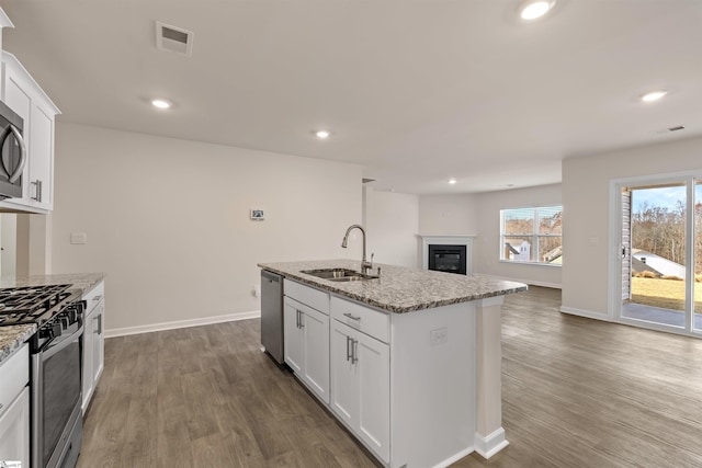 kitchen with light stone counters, stainless steel appliances, a kitchen island with sink, sink, and white cabinets