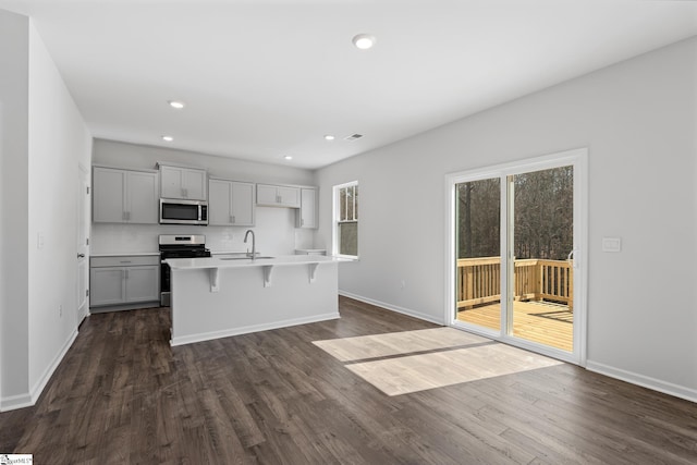 kitchen with a kitchen bar, an island with sink, dark wood-style floors, recessed lighting, and stainless steel appliances