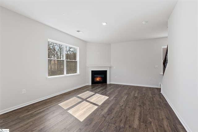 unfurnished living room with a glass covered fireplace, visible vents, dark wood-type flooring, and baseboards