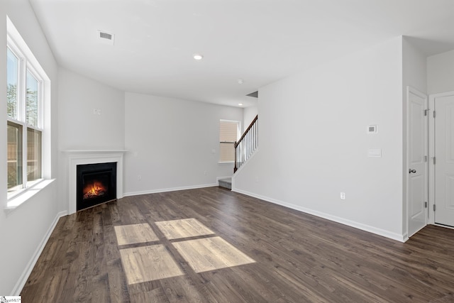 unfurnished living room featuring visible vents, a lit fireplace, dark wood finished floors, and stairway