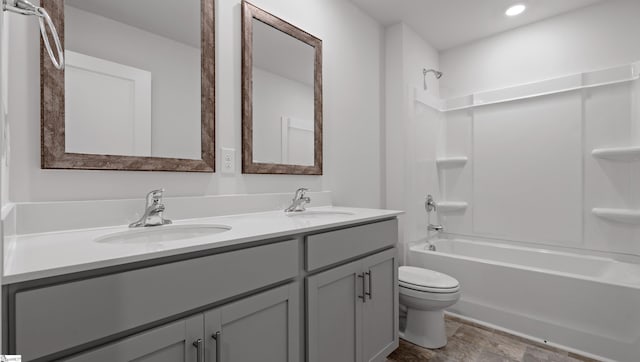 bathroom with double vanity, washtub / shower combination, toilet, and a sink