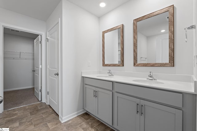 full bathroom with double vanity, a walk in closet, baseboards, and a sink