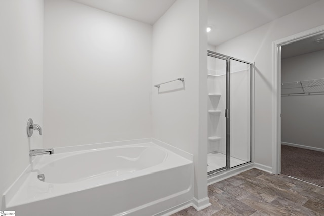 bathroom featuring a shower stall, a spacious closet, a garden tub, and baseboards