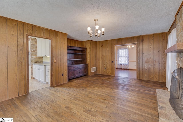 unfurnished living room with wooden walls, hardwood / wood-style floors, and a notable chandelier