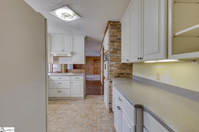 kitchen with white cabinets, a textured ceiling, wooden walls, and white oven