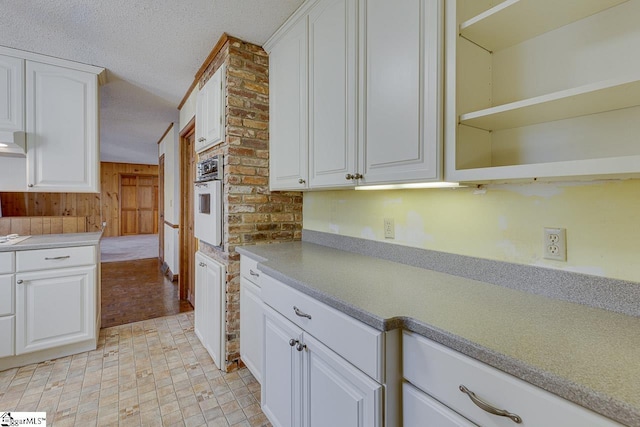 kitchen featuring white cabinets, a textured ceiling, wooden walls, and white oven