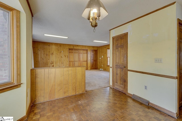 unfurnished room with a wealth of natural light, wooden walls, a textured ceiling, and parquet flooring