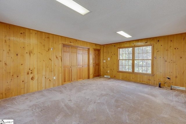 empty room featuring wood walls, carpet floors, and a textured ceiling