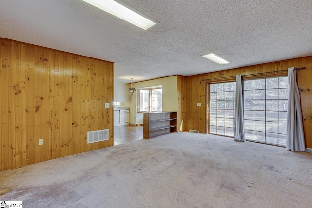 unfurnished living room featuring wooden walls, carpet flooring, and a wealth of natural light