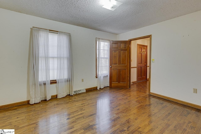 unfurnished room with a textured ceiling, hardwood / wood-style flooring, and a healthy amount of sunlight