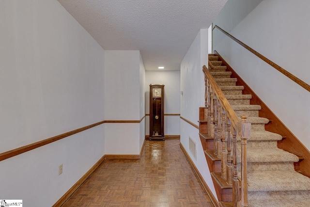 stairway featuring a textured ceiling and parquet flooring