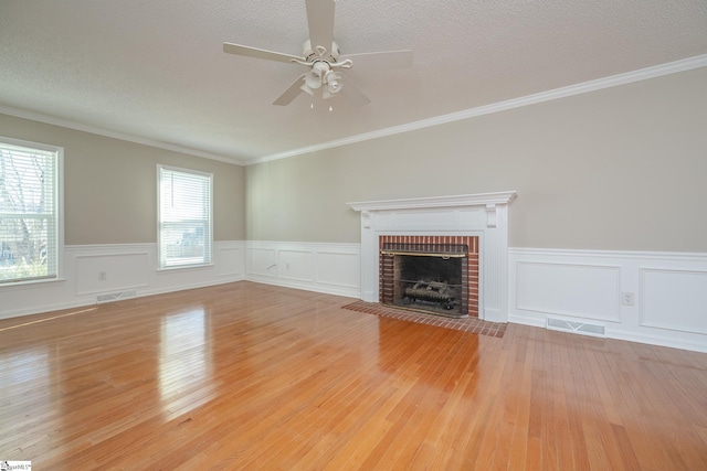 unfurnished living room featuring a brick fireplace, ornamental molding, a healthy amount of sunlight, and light hardwood / wood-style floors