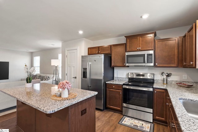 kitchen featuring a breakfast bar, a center island, dark hardwood / wood-style floors, light stone countertops, and appliances with stainless steel finishes