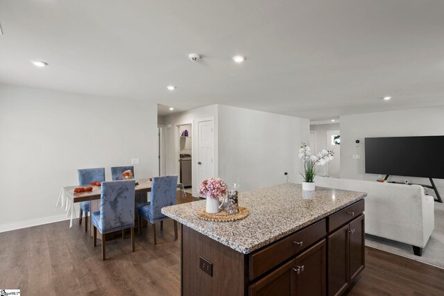 kitchen featuring light stone counters, dark brown cabinets, a kitchen island, and dark wood-type flooring