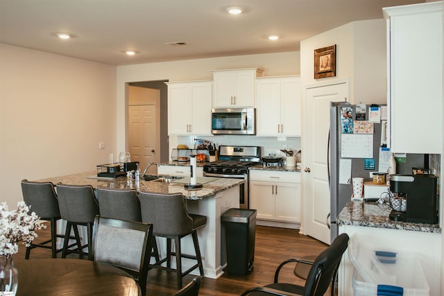 kitchen featuring white cabinetry, dark hardwood / wood-style flooring, dark stone countertops, a kitchen bar, and appliances with stainless steel finishes