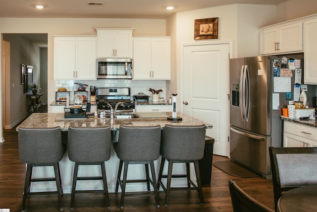 kitchen with appliances with stainless steel finishes, a center island with sink, and white cabinetry