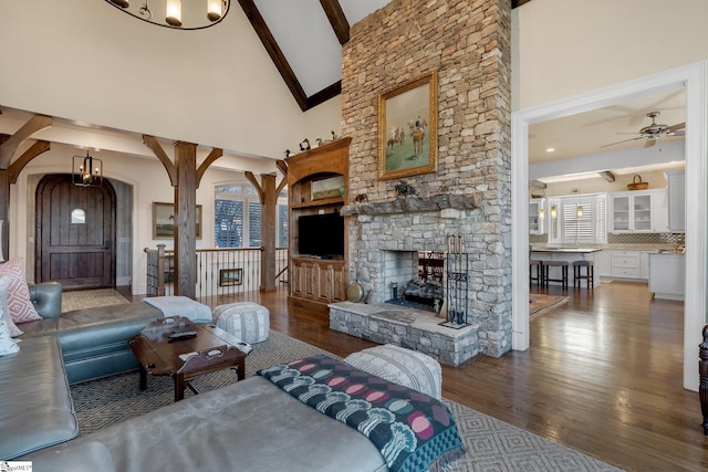 living room with dark hardwood / wood-style flooring, ceiling fan with notable chandelier, high vaulted ceiling, beamed ceiling, and a fireplace