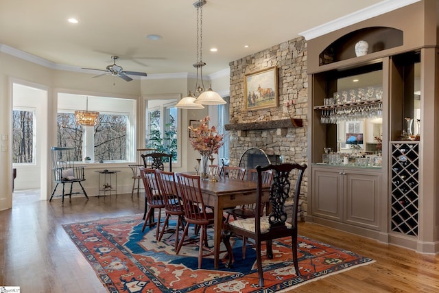 dining room featuring a stone fireplace, ornamental molding, and hardwood / wood-style flooring