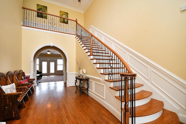 stairs with crown molding, french doors, hardwood / wood-style floors, and a high ceiling