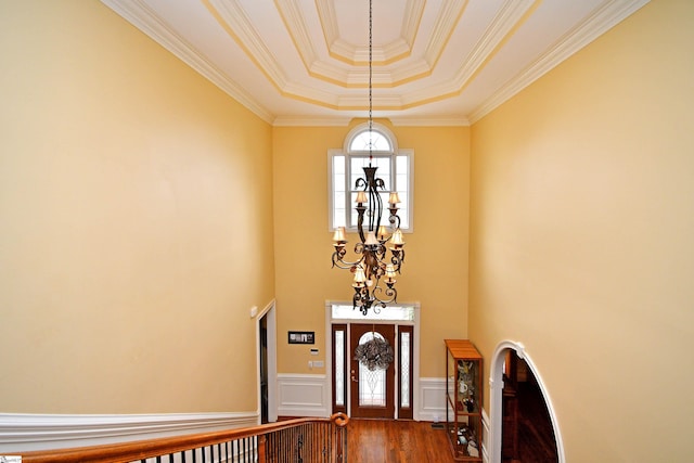 foyer entrance featuring wood-type flooring, a tray ceiling, crown molding, and a notable chandelier