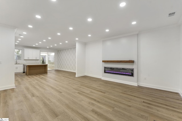 unfurnished living room with sink, light hardwood / wood-style flooring, and ornamental molding