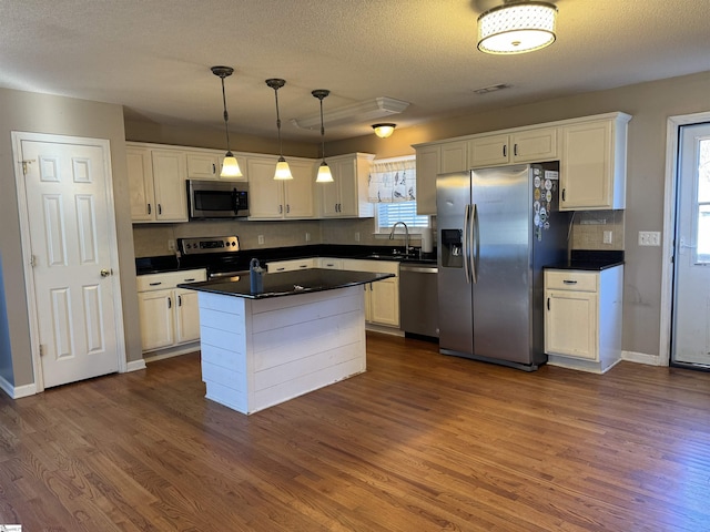 kitchen featuring dark wood-type flooring, white cabinets, stainless steel appliances, and decorative light fixtures