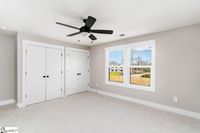 unfurnished bedroom with two closets, light colored carpet, and ceiling fan