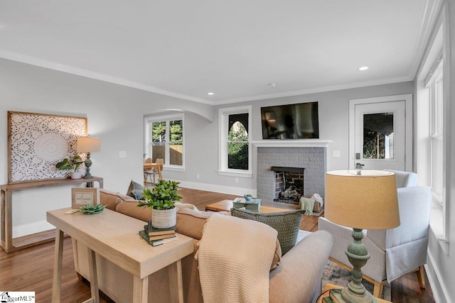 living room featuring hardwood / wood-style flooring, crown molding, and a brick fireplace