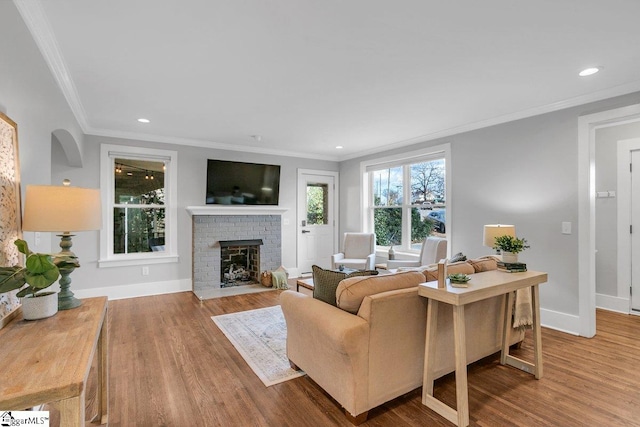 living room featuring hardwood / wood-style flooring, ornamental molding, and a brick fireplace