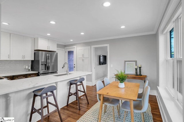 kitchen with backsplash, white cabinets, sink, stainless steel refrigerator with ice dispenser, and light stone counters