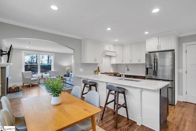 kitchen with kitchen peninsula, stainless steel refrigerator with ice dispenser, ornamental molding, sink, and white cabinetry