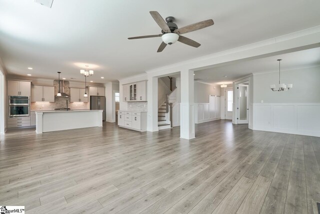 unfurnished living room featuring a healthy amount of sunlight, light hardwood / wood-style floors, ceiling fan with notable chandelier, and ornamental molding