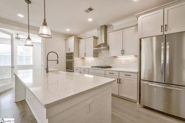 kitchen featuring light stone counters, stainless steel appliances, sink, wall chimney range hood, and decorative light fixtures