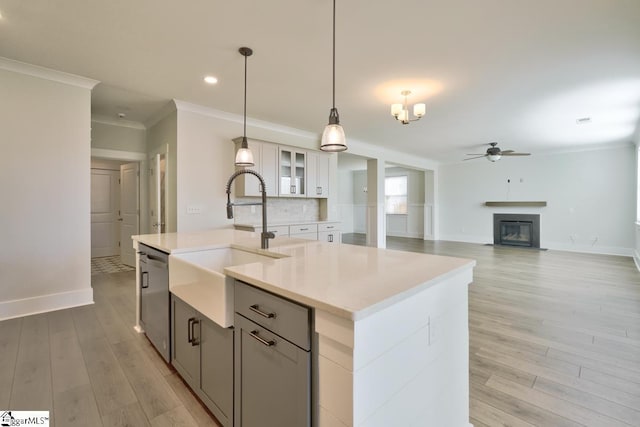 kitchen with dishwasher, a kitchen island with sink, sink, ornamental molding, and decorative light fixtures