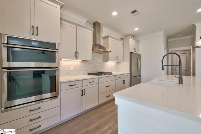 kitchen featuring decorative backsplash, appliances with stainless steel finishes, wall chimney exhaust hood, sink, and light hardwood / wood-style floors