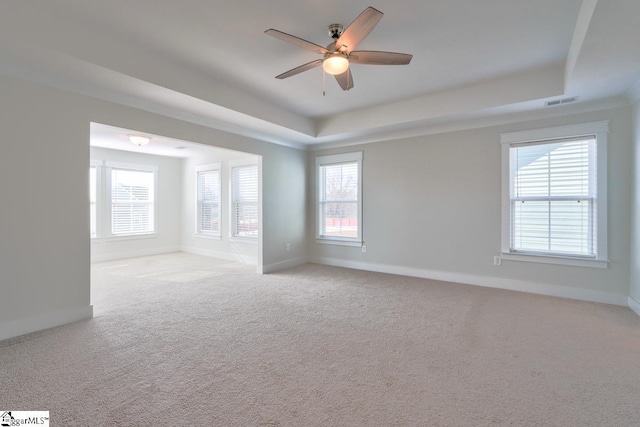 carpeted empty room with ceiling fan, plenty of natural light, and a tray ceiling