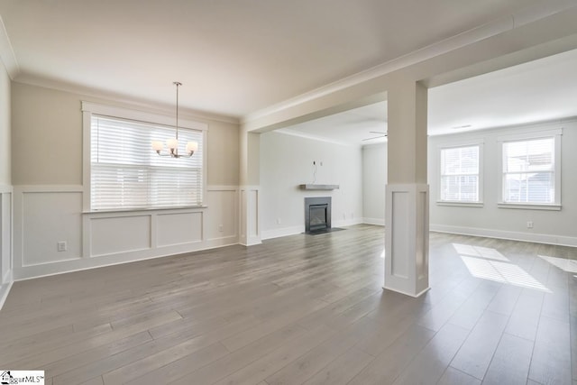 unfurnished living room with wood-type flooring, ceiling fan with notable chandelier, and crown molding