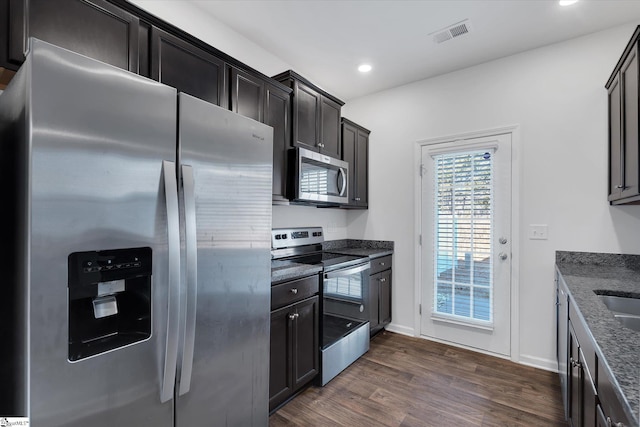 kitchen featuring sink, dark wood-type flooring, appliances with stainless steel finishes, and dark stone counters