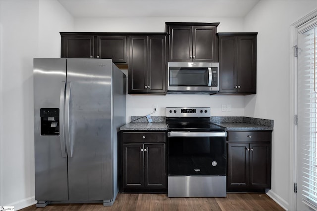 kitchen with dark stone counters, dark brown cabinetry, stainless steel appliances, and dark hardwood / wood-style floors