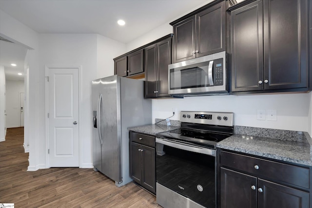 kitchen featuring dark stone countertops, dark hardwood / wood-style flooring, dark brown cabinets, and appliances with stainless steel finishes