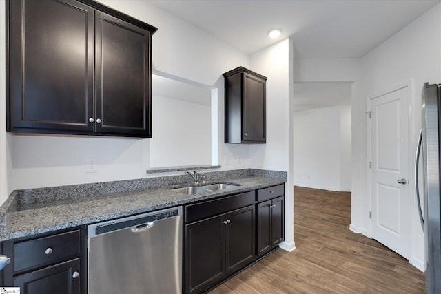 kitchen with sink, dark stone countertops, wood-type flooring, dark brown cabinets, and appliances with stainless steel finishes